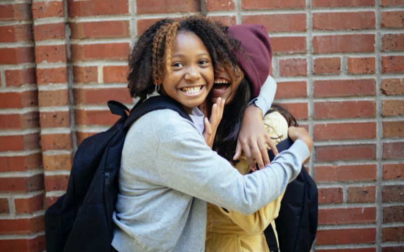 Two girls share a warm embrace outside a school