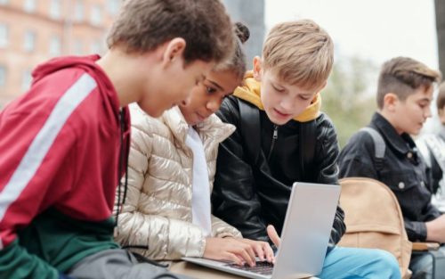 Three boys gather around a laptop outside