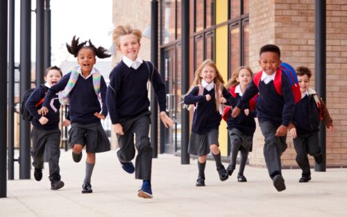 Primary school children in unforms run smiling towards the camera